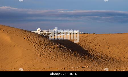 Espagne, îles Canaries, Grande Canarie, côte sud, Maspalomas, espace dune, lumière du soir, dune avec empreintes de pas en premier plan, immense hôtel de luxe blanc derrière les dunes, ciel bleu, nuages gris-bleu Banque D'Images