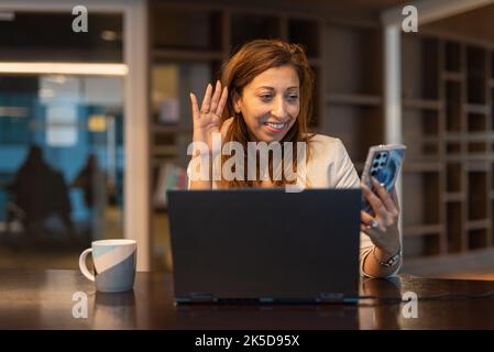 Portrait d'une femme d'affaires utilisant un ordinateur portable et un téléphone portable la nuit dans une prise de vue horizontale au bureau Banque D'Images