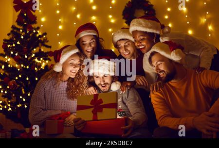 Heureux diverses personnes ouvrant boîte cadeau avec beau cadeau magique de Noël à l'intérieur Banque D'Images