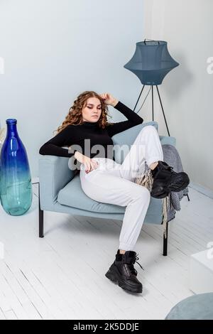 Une belle femme aux longs cheveux bouclés dans un pull noir, un pantalon blanc, des baskets en cuir noir. Nouvelle collection de chaussures décontractées pour Femme Banque D'Images