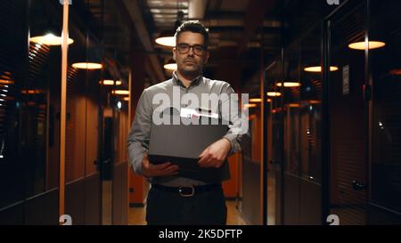 A tiré un homme contrarié en costume marchant dans le couloir du bureau, tenant une boîte avec des livres et des trucs personnels, disant Au revoir à des collègues, regardant l'appareil photo. Employé de sexe masculin quittant la société de marketing Banque D'Images