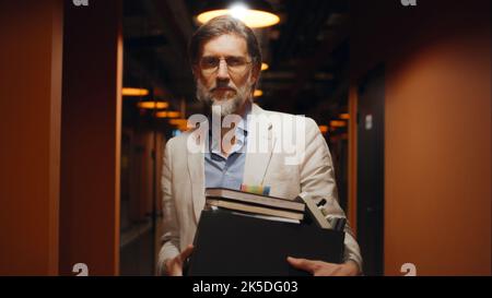 Homme d'affaires mature et réussi en costume et lunettes debout dans le couloir du bureau, souriant, regardant la caméra. Employé de bureau masculin dans le couloir de la société de marketing moderne centre d'affaires Banque D'Images
