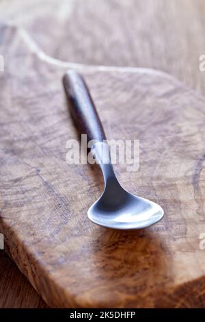 Une cuillère à café vide faite de bois et de métal sur une planche à découper en bois d'olive - vue rapprochée Banque D'Images