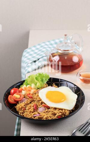 Indomie Goreng ou Mie Goreng, indonésien populaire Instant Noodle. Servi avec un œuf de poule, de la tomate et de la laitue Banque D'Images