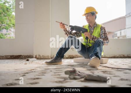 Ouvrier de construction utilisant un marteau à inertie électrique pour percer des trous avant de verser le sol pour être fort sur le chantier de construction Banque D'Images