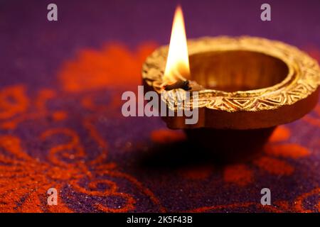 Happy Diwali Festival of Lights fond violet avec lumière dorée traditionnelle à l'huile d'argile Diya allumé sur orange Rangoli design pendant Deepavali. Banque D'Images