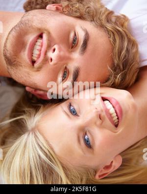 C'est un couple heureux. Portrait d'un jeune couple allongé au lit avec leur tête ensemble. Banque D'Images