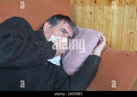 Homme malade allongé sur le canapé avec un mouchoir dans son nez. Banque D'Images