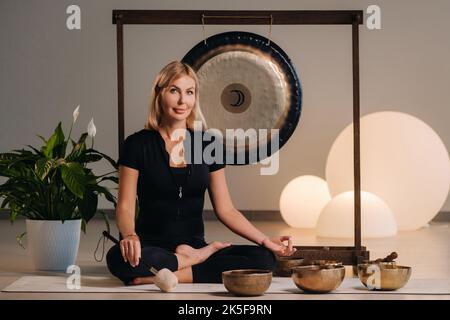 Une femme est assise avec un marteau et à côté d'un gong et de bols tibétains à l'intérieur. Banque D'Images