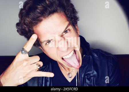Rock n Roll. Gros plan d'un jeune homme qui colle sa langue et fait des gestes de main entourés d'un halo de lumière. Banque D'Images
