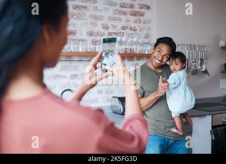 Famille, soins et mère avec téléphone pour la photo de père et de bébé avec le syndrome de Down dans le salon de leur maison. Maman prenant une photo d'un heureux Banque D'Images