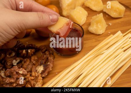 Quelqu'un trempent un morceau de fromage dans le miel sur un fond de variétés variées de fromage Banque D'Images