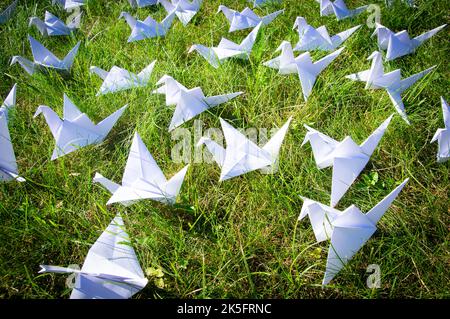 Grues Origami pliées japonaises sur de l'herbe fraîche. Des centaines d'oiseaux en papier faits main sur un terrain vert avec espace de copie. 1000 mille grue tsuru sujet de sculpture. Symbole de paix, de foi, de santé, de souhaits et d'espoir Banque D'Images