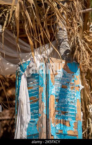 volets en bois peints sur un bâtiment de plage délabré en bois flotté et en feuilles de palmiers. Banque D'Images