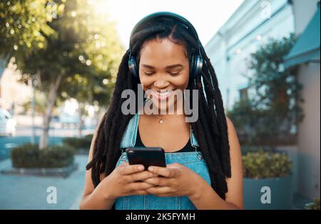 Femme noire, casque audio et téléphone avec sourire pour 5g communications et diffusion audio en extérieur. Bonne femme africaine souriante, à l'écoute Banque D'Images