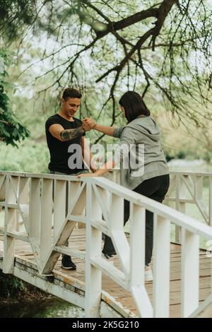 Joli couple qui se fait serrer la main et rire en se tenant sur le pont blanc dans le parc Banque D'Images