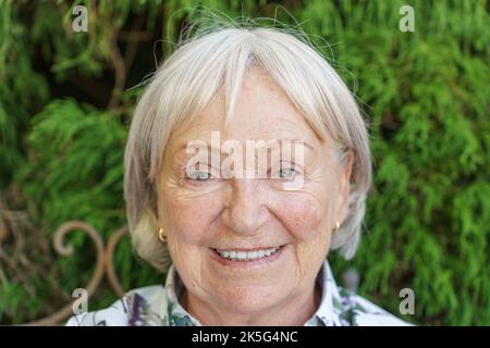 Portrait en tête d'une femme sénior attirante donnant à l'appareil photo un sourire chaleureux et enrayant à l'extérieur dans un jardin Banque D'Images