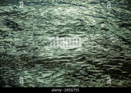 Texture formée par les vagues arrondies et courbées de l'eau et les vagues de la mer avec des tons gris et bleutés et des réflexions de lumière Banque D'Images