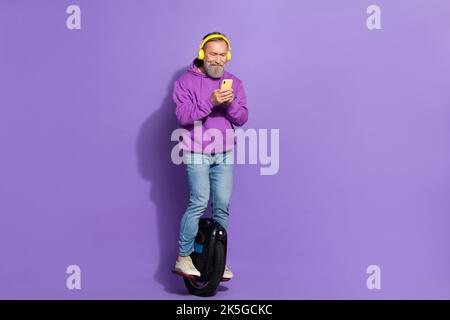 Portrait de l'ancien retraité positif homme en bonne santé porter le pull à capuche violet conduite monotalon écouter la liste de lecture isolée sur fond violet couleur Banque D'Images