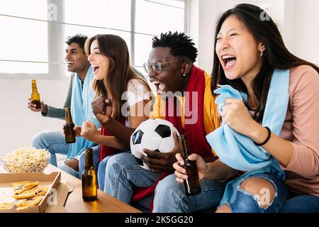 Des jeunes fans de football multiethniques soutiennent leur équipe nationale à la télévision Banque D'Images