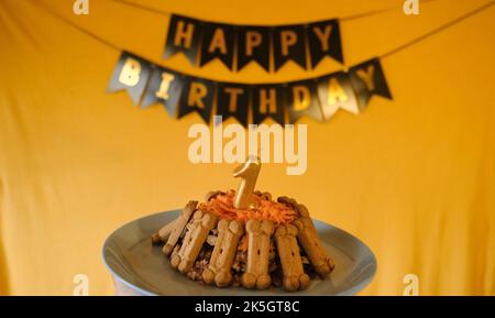 Concept de l'anniversaire du chien. Gâteau pour animaux de compagnie fait de biscuits en forme d'os de viande, carottes et nombre d'or de 1 bougie. Drapeaux noirs avec inscription ha Banque D'Images