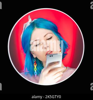 Divertissement par téléphone. Chat mobile. Style de vie millénaire. Attrayante femme calme message texte sur smartphone sur fond rouge dans le visage rond noir avat Banque D'Images