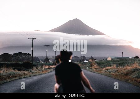 un jeune caucasien peu concentré se broutant sur son dos en prenant une photo de l'impressionnante montagne et des nuages avec son appareil photo et son trépied au milieu Banque D'Images