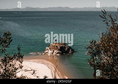 petite île curieuse de pierre et de roche sur la rive de la plage de sable blanc avec un peu de végétation sur le dessus et donnant sur les montagnes dans un calme Banque D'Images