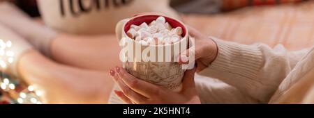tasse de chocolat chaud ou de boisson au café avec guimauves en femme tenant les mains de la femme en pull relaxant et profiter des vacances au lit Banque D'Images