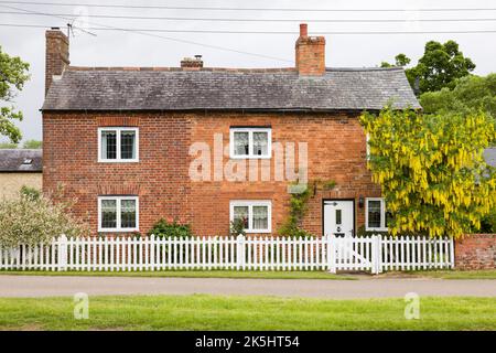 NORTHAMPTONSHIRE, Royaume-Uni - 25 mai 2022. Ancienne maison de campagne en briques avec clôture de piquetage blanche Banque D'Images