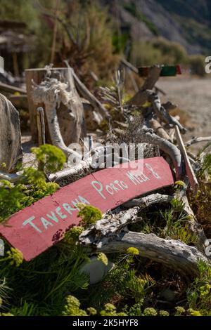 affiche de taverne grecque lavée sur une plage de sable sur zante ou zakynthos, flotsam et jetsam sur la plage en grèce avec des panneaux en bois et des débris hauts et secs. Banque D'Images