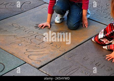 Une femme prend la taille de ses mains dans les empreintes de la star de cinéma Marylin Monroe dans la cour en ciment et la plaza du théâtre chinois de Grauman à Hollywood Banque D'Images