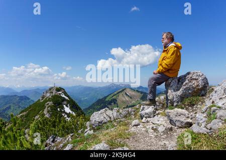 Randonneur, âgé de 63 ans, reposant sur le sommet du Buchstein, en arrière-plan Rossstein et Benediktenwand, Kreuth, Mangfall Mountains, haute-Bavière Banque D'Images