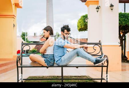 Un couple contrarié assis dos à dos sur un banc de parc. Concept d'un couple arguant dans un parc. Un jeune couple contrarié, assis à l'arrière à l'extérieur, jeune Banque D'Images