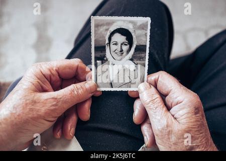 VERS 1970 : mains de femme âgée tenant une photo vintage, noire et blanche de la jeune femme. Concept de passage du temps Banque D'Images