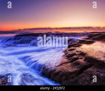 Lever de soleil pittoresque et coloré sur la plage de baleines des plages du nord de Sydney, sur la côte Pacifique de l'Australie, avec des rochers débordant à gauche. Banque D'Images