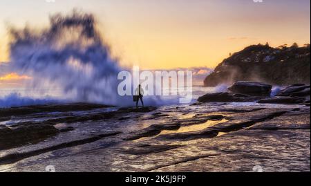 Une énorme vague qui frappe des rochers sur la plage de Whale de la côte du Pacifique à Sydney, en Australie, avec une planche à voile floue face à l'océan. Banque D'Images