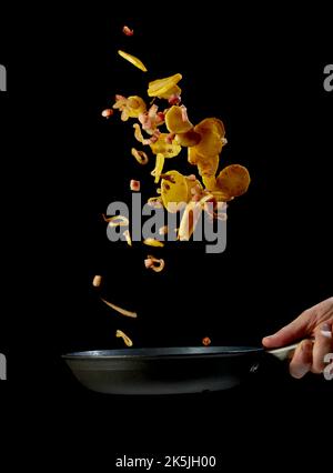 Préparez un délicieux dîner sur fond noir avec un chef masculin méconnu qui tient une poêle à frire et qui prépare des tranches de pommes de terre et du bacon Banque D'Images