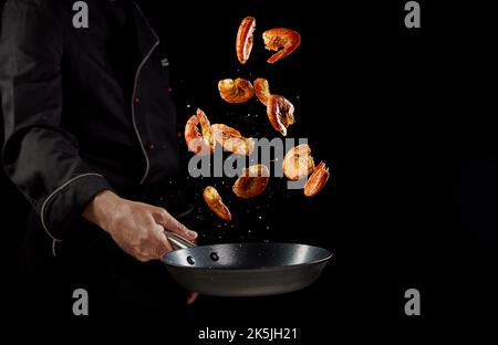 Croiser un chef anonyme qui lance des crevettes dans une poêle tout en cuisant un délicieux dîner avec des fruits de mer sur fond noir Banque D'Images