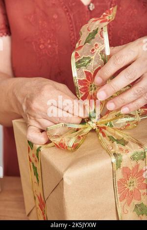 Gros plan sur les mains des femmes faisant un noeud avec un ruban décoratif pour décorer un cadeau de Noël. Concept de vacances enveloppantes présente. Banque D'Images