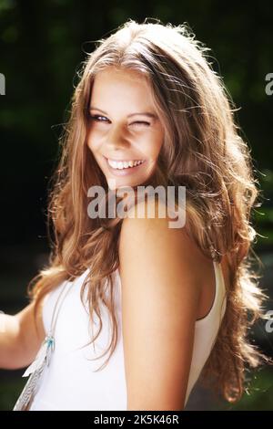 Amusant et flirté. Portrait d'une belle jeune femme qui vous fait un clin d'œil dans une forêt verte. Banque D'Images