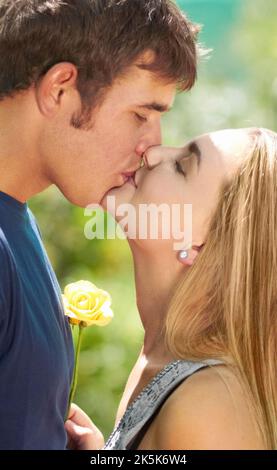 Soleil embrassa l'amour. Un jeune couple embrassant tandis que la femme tient une fleur. Banque D'Images