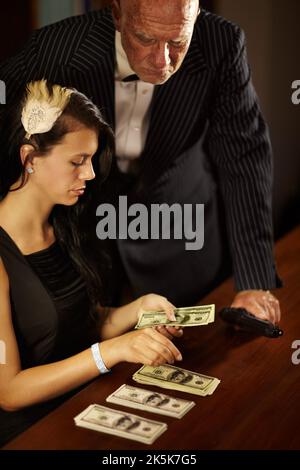 Surveiller leurs gains mal acquis. Une jeune femme compte de l'argent comme un patron de foule regarde au-dessus d'elle. Banque D'Images