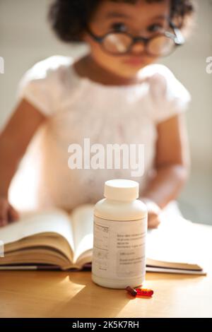 Le médicament a beaucoup d'utilisations. Une petite fille à la maison seule avec des pilules sur la table en face d'elle. Banque D'Images