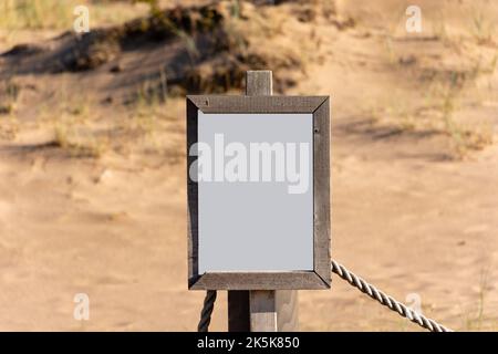 Panneau blanc vide avec cadre en bois partiellement cassé sur une plage de sable Banque D'Images