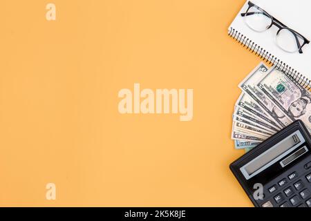 Calculatrice, argent et bloc-notes sur fond orange, espace copie. Banque D'Images
