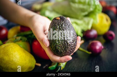 Avocat dans une main femelle sur un fond flou avec des légumes. Banque D'Images