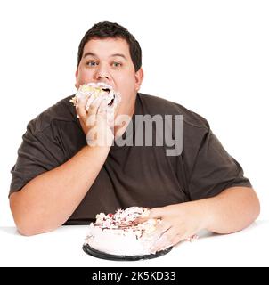 Manger du gâteau en un temps record. Un jeune homme obèse farce un gâteau sur son visage et ne pas être trop dineux à ce sujet. Banque D'Images