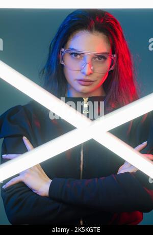 Femme cyberpunk. Portrait au néon. Mode technique. Brave et confiante héros féminin dans des lunettes avec bras croisés dans une lumière néon rouge avec laser LED blanc illumina Banque D'Images