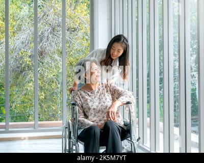 Bonne femme asiatique âgée, mère ou grands-parents en fauteuil roulant prenant soin par le soignant, souriant jeune femme, fille ou petit-enfant soutenant à h Banque D'Images